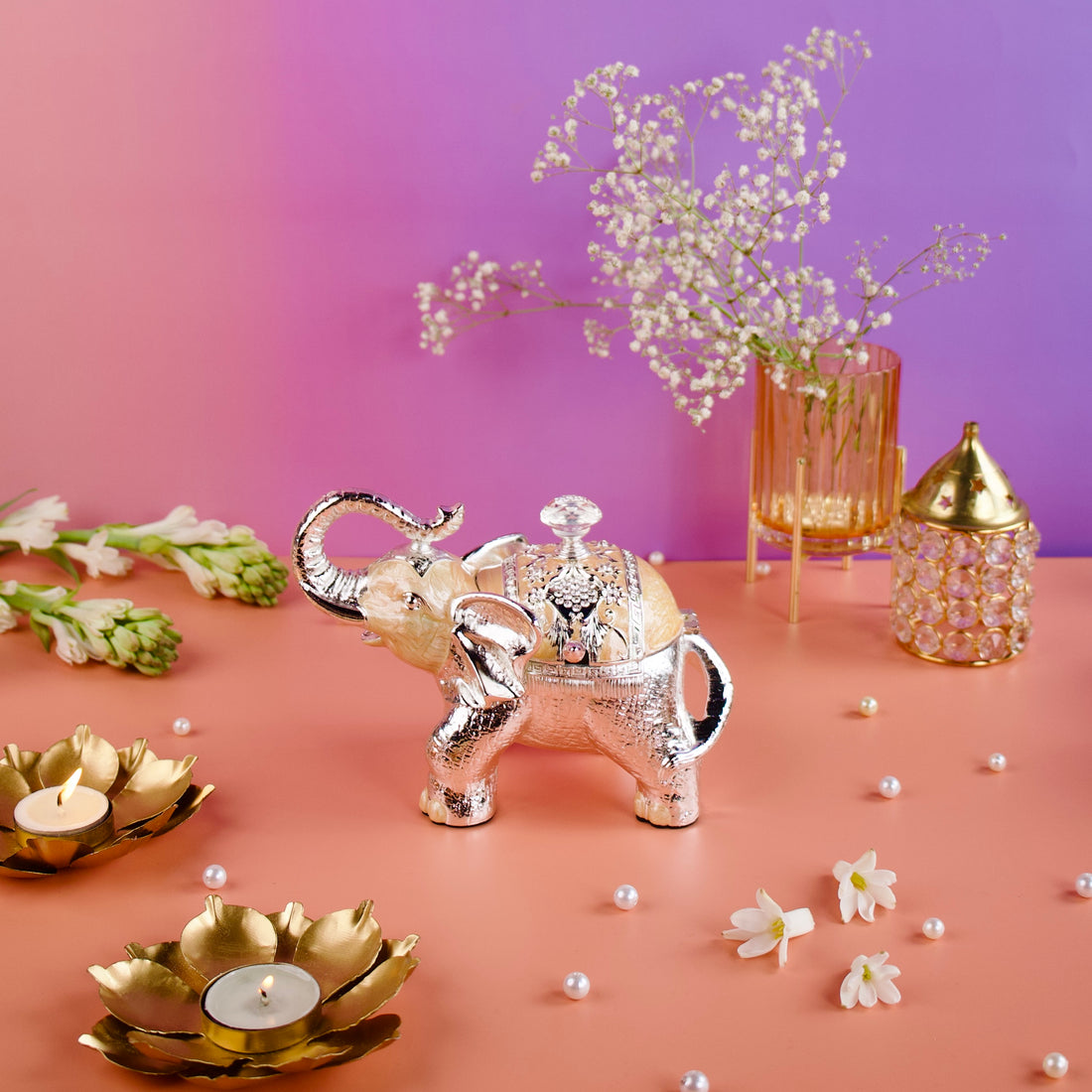 Decorative elephant teapot with flowers and candles on a pink surface