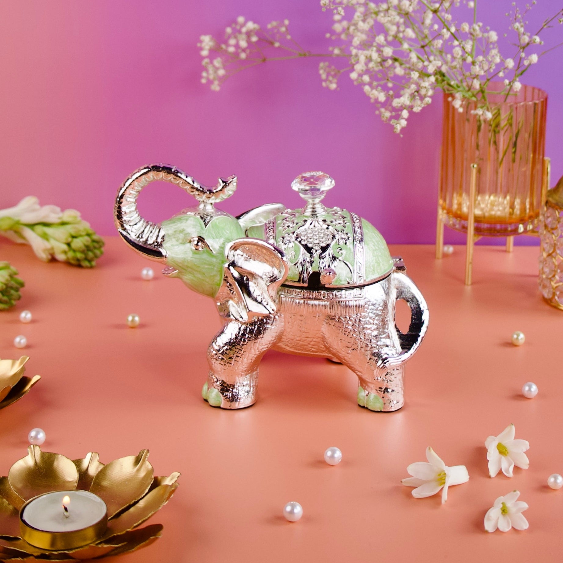 Decorative elephant teapot with flowers and candles on a pink surface